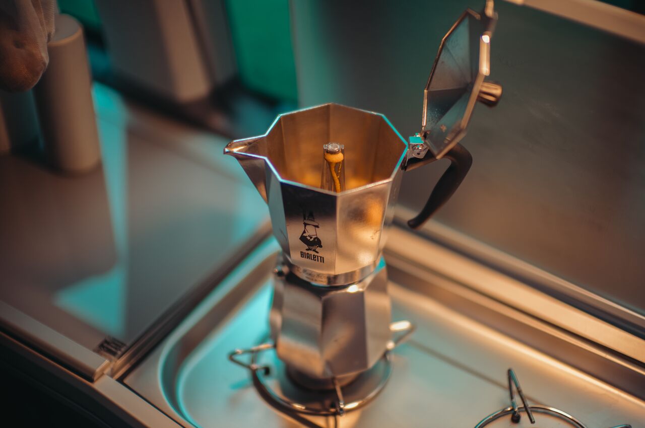 Coffee streaming into the upper chamber of a moka pot on a stove inside a van.