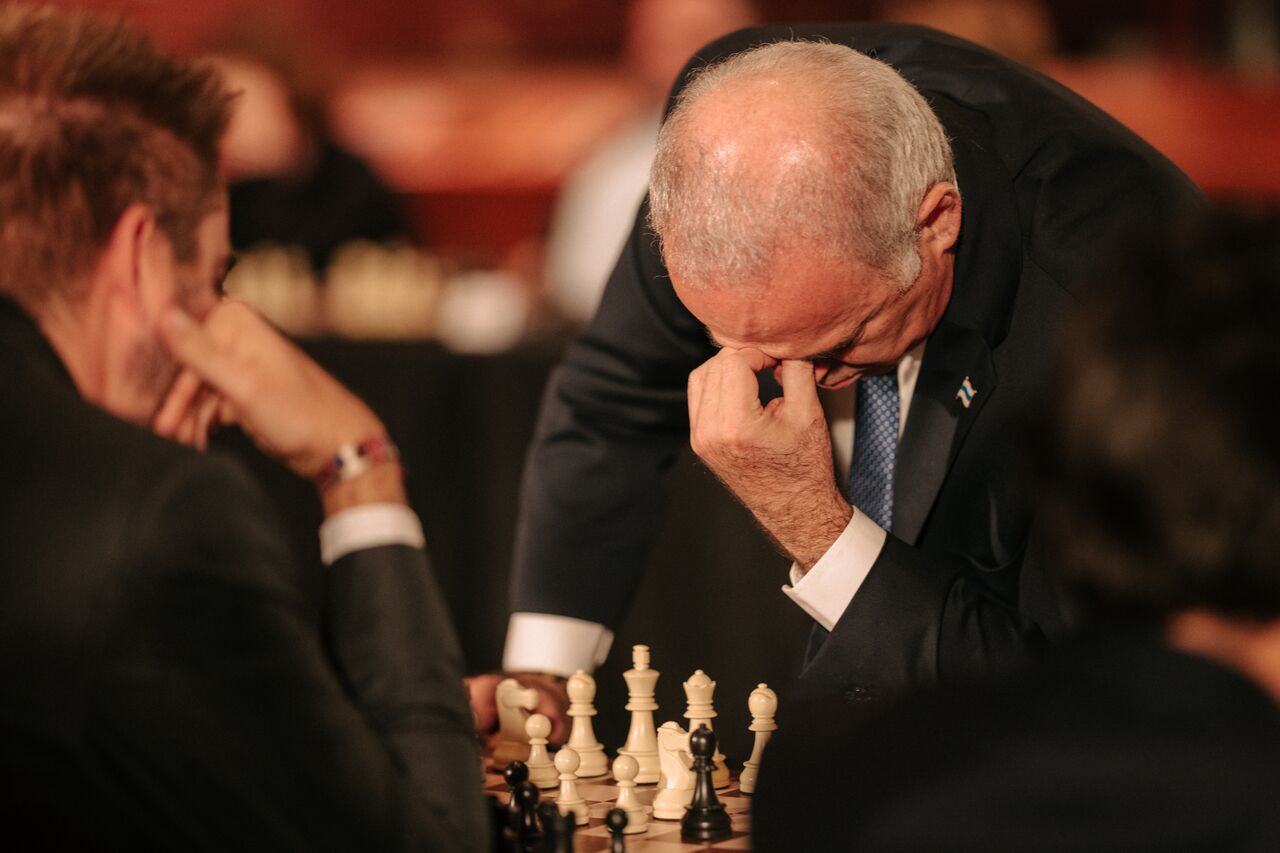 Kasparov leans over the chessboard, thinking deeply during a game.