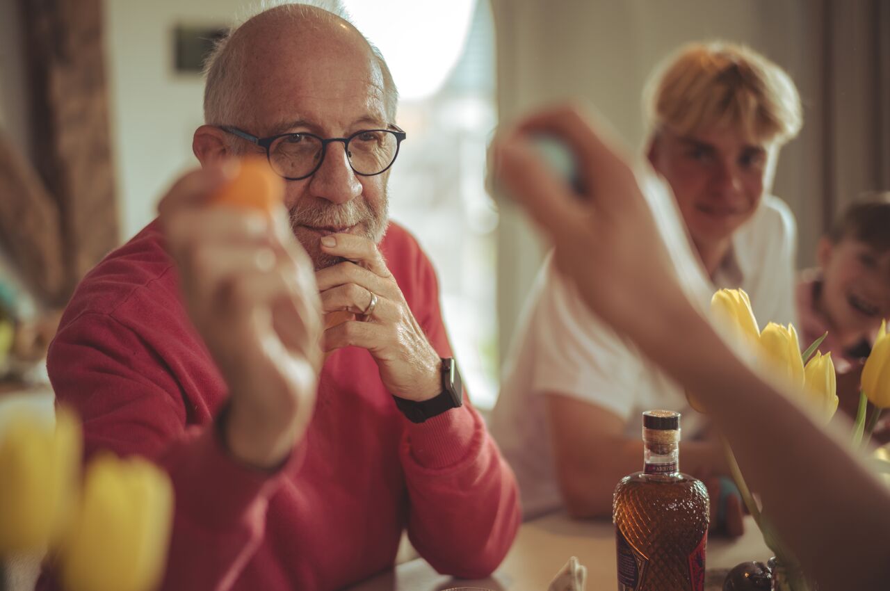 A man holds up a brightly colored Easter egg with a quiet smile, ready to tap it against another.