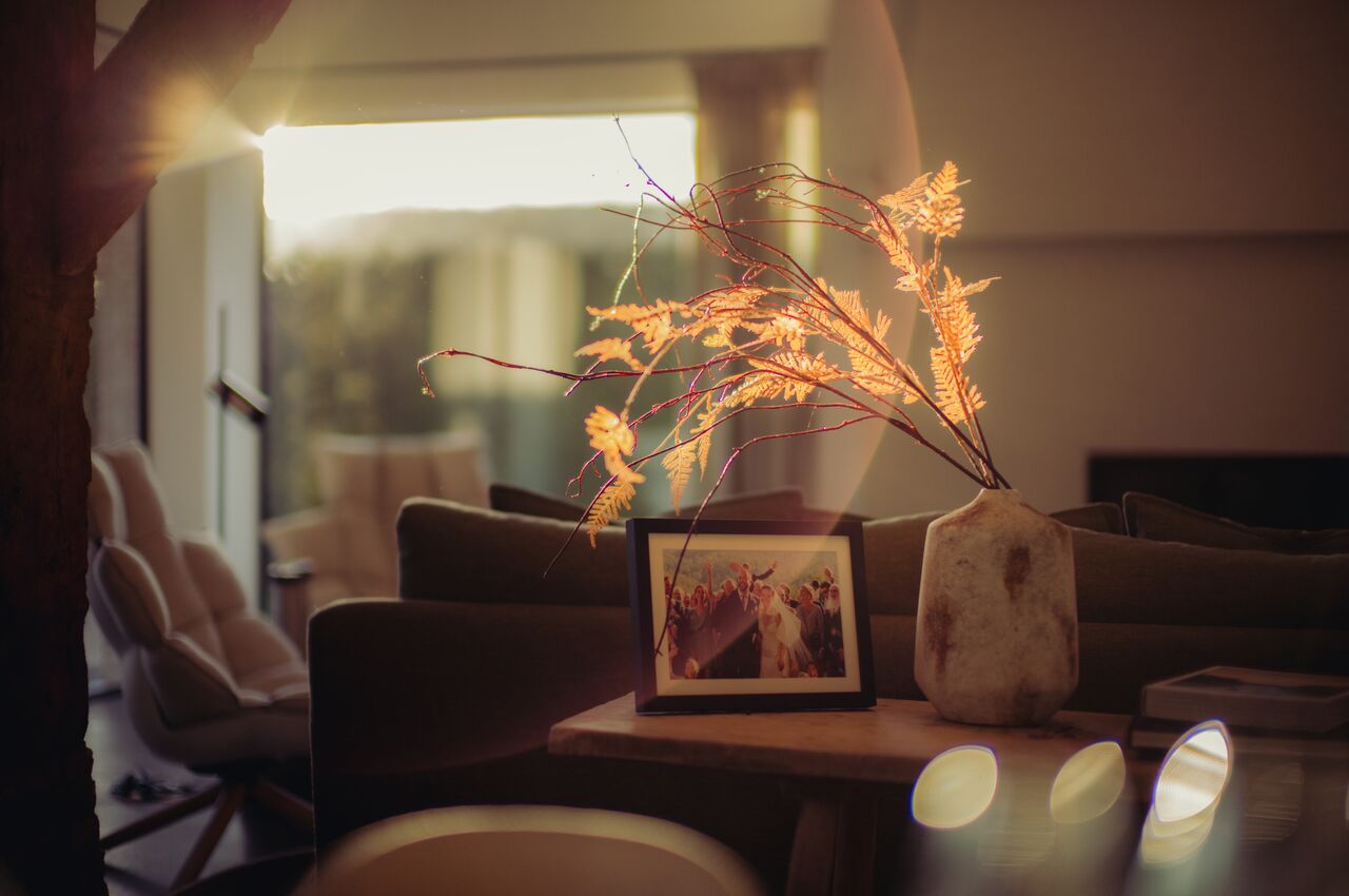 Warm fall light fills a quiet living room, illuminating a vase of dried branches and a framed photo on a wooden table.