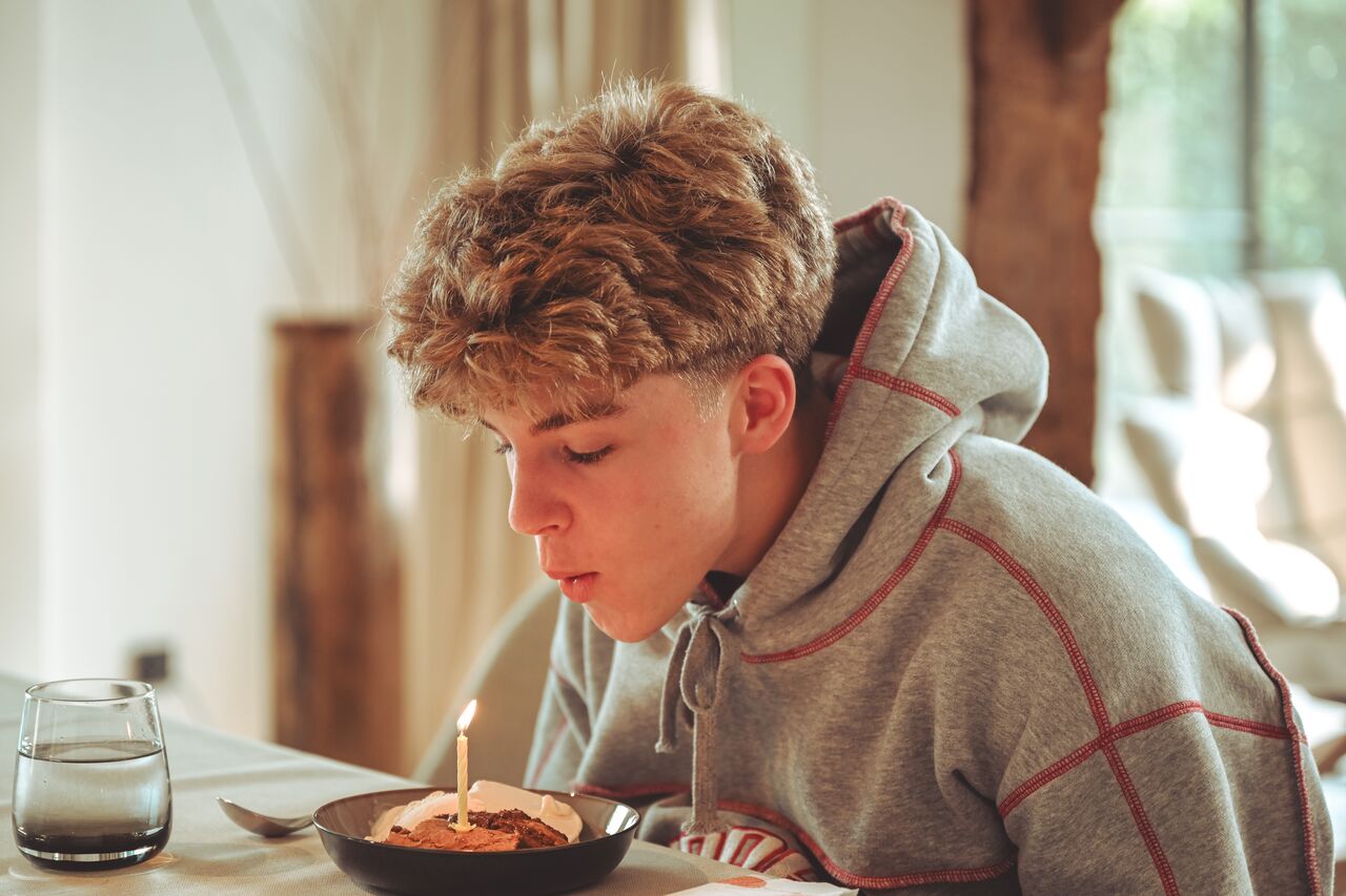 A person leans forward to blow out a candle on a warm cookie topped with ice cream.
