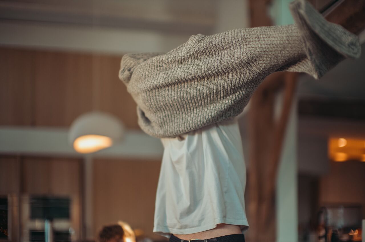 A young man pulling a new sweater over his head, mid-motion.