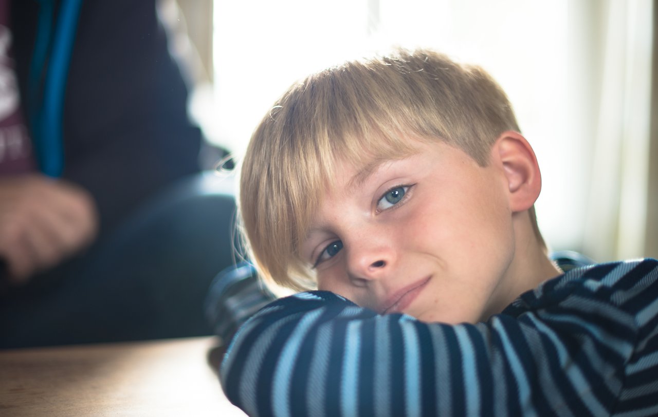 A young boy with blond hair rests his head on his arms, gazing softly at the camera.
