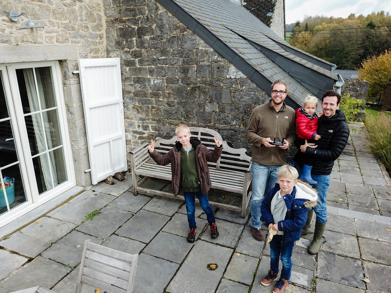 A group of people standing on a patio, smiling and waving at a drone camera.