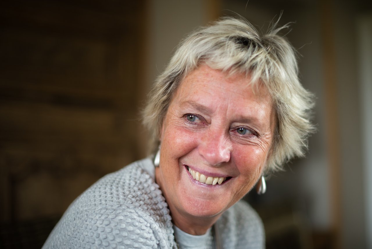 A woman with short blonde hair and a gray sweater smiles while looking to the side.