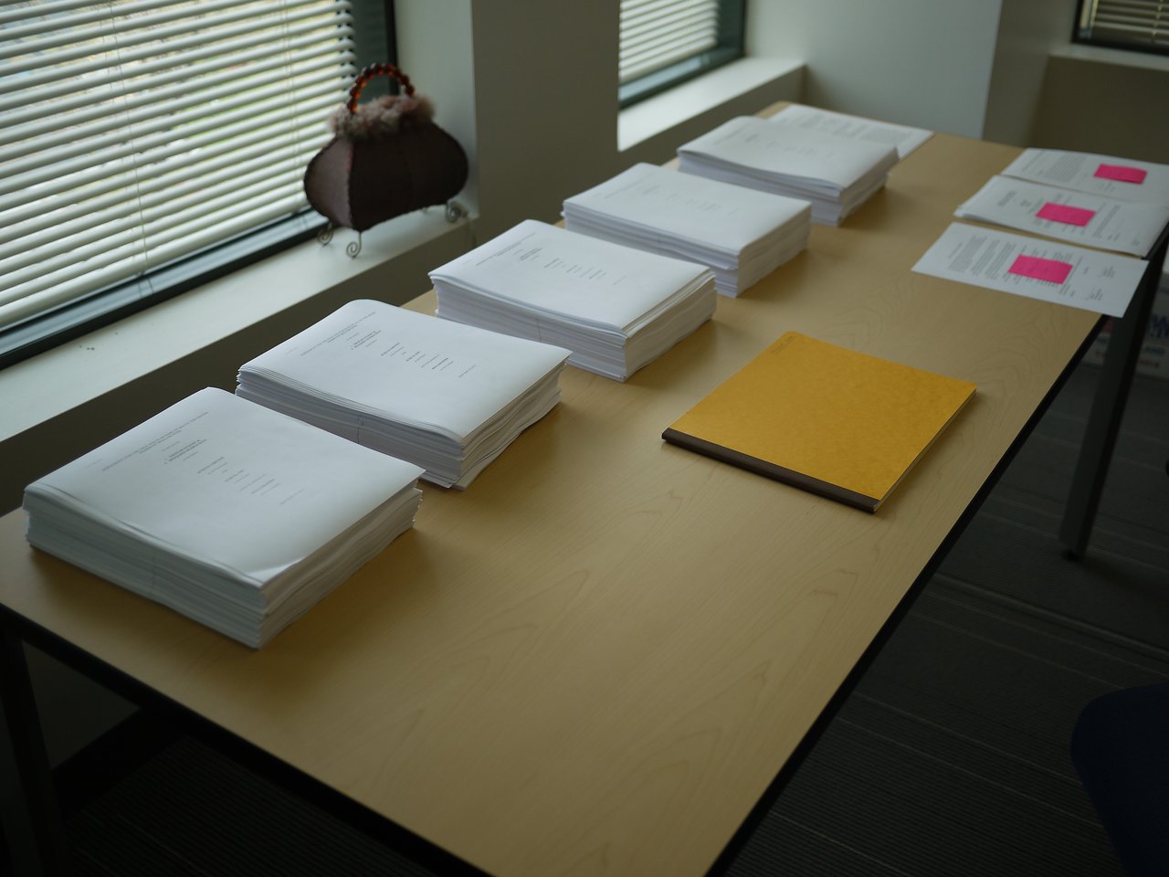 Stacks of printed documents and a folder are neatly arranged on a table in an office setting.