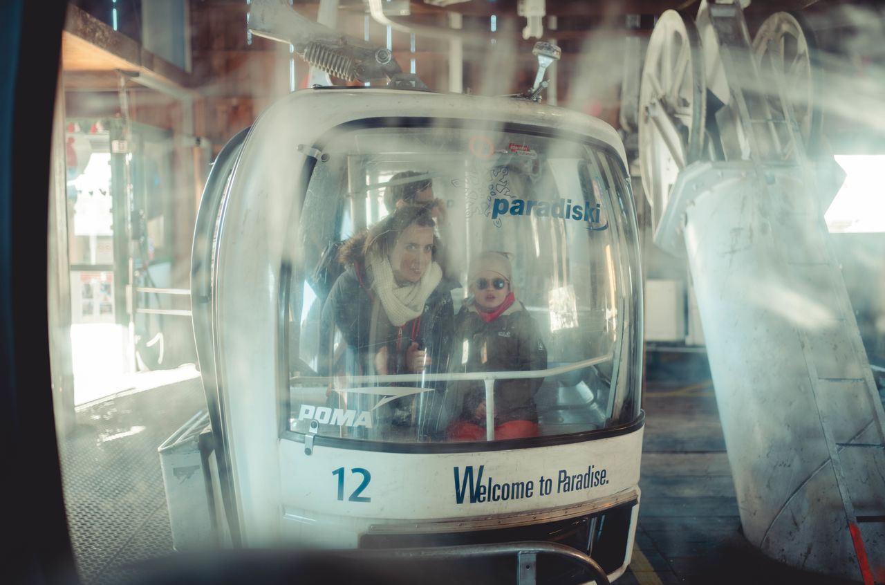 A family sits inside a ski gondola, dressed in winter clothing, preparing for a ride up the mountain.