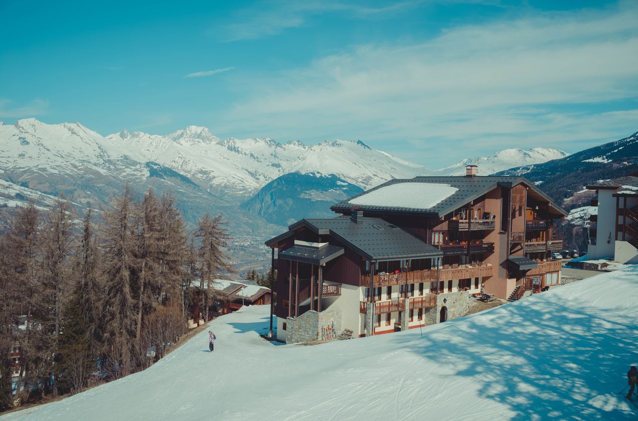 A large wooden lodge with snow-covered mountains in the background.