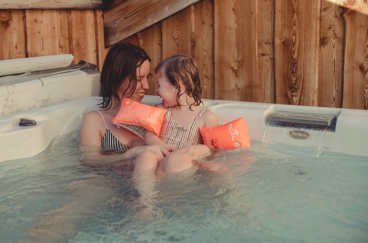 A woman and a young child sit in a hot tub, smiling at each other.