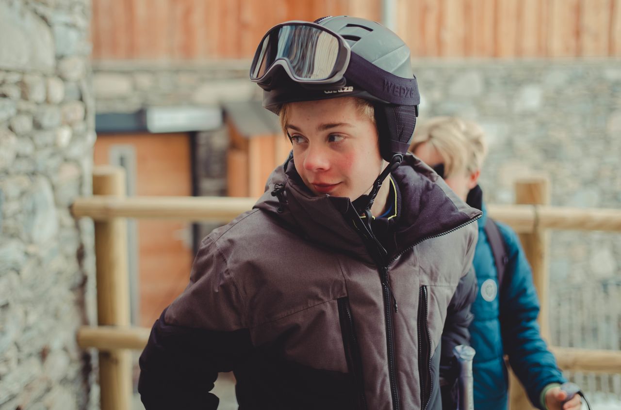 A boy wearing a ski helmet and goggles looks to the side, dressed in a winter jacket.