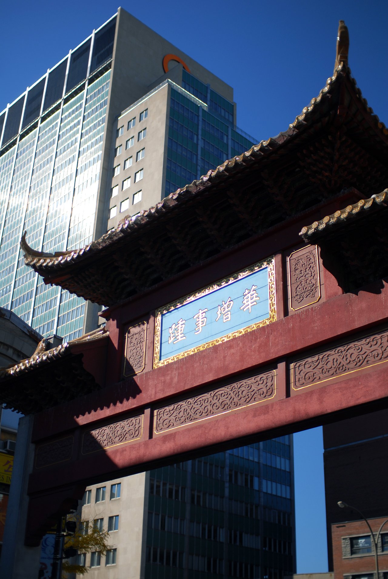 A traditional Chinese gate with decorative carvings and Chinese characters stands in front of modern glass buildings in Montreal.