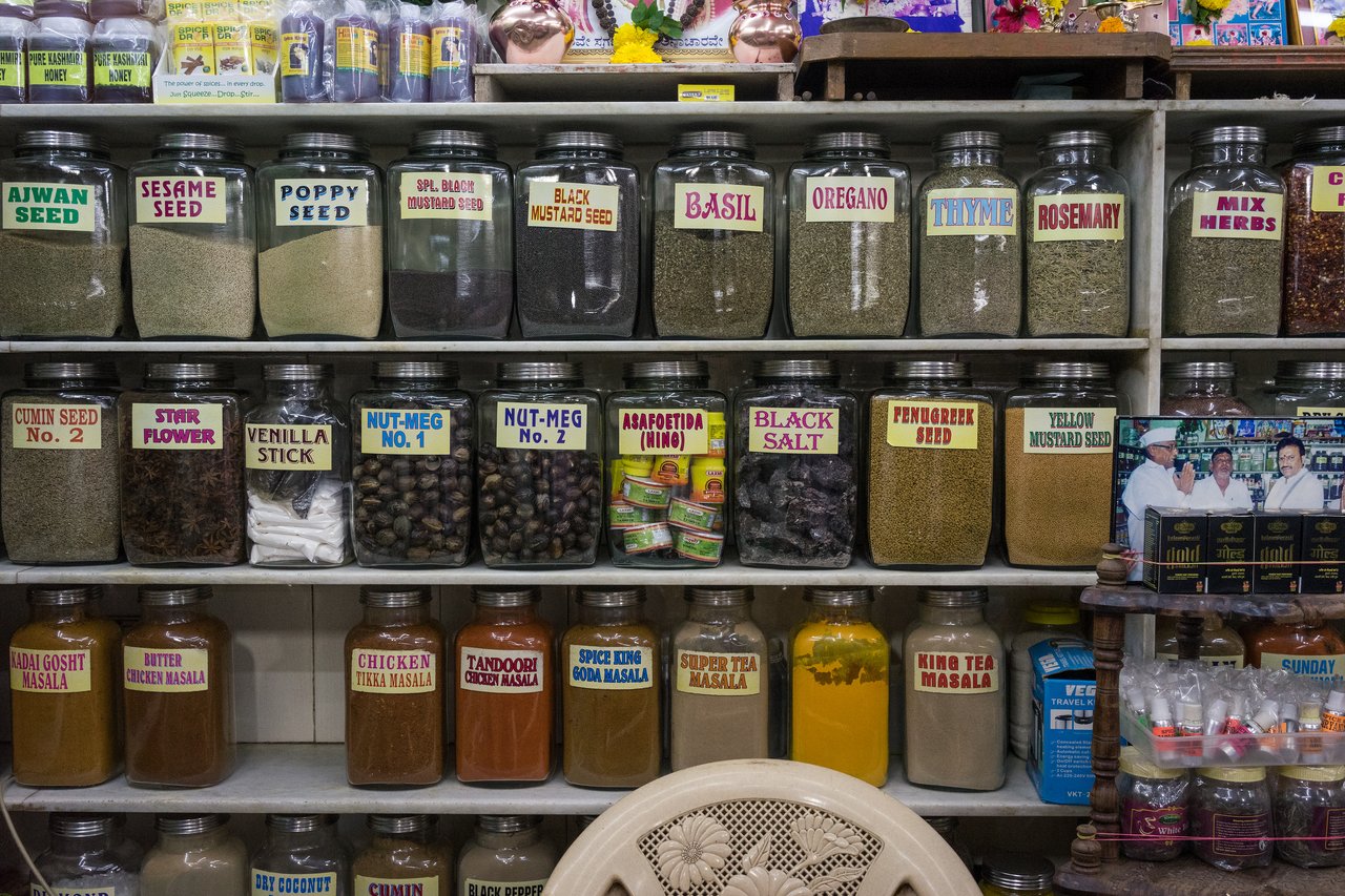 Glass jars filled with various spices and herbs are neatly arranged on shelves in a store.