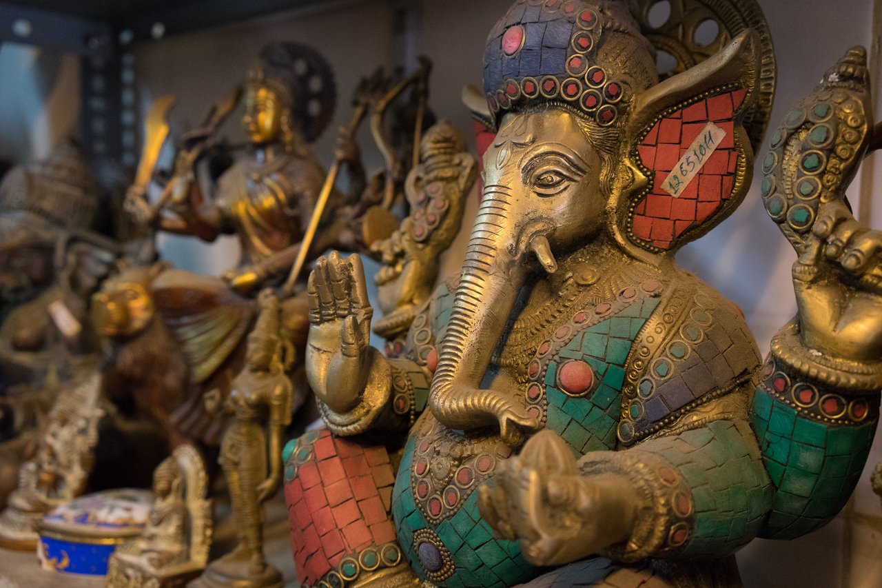 A colorful statue of Ganesha with one hand raised, surrounded by other Hindu deity statues on a shelf.