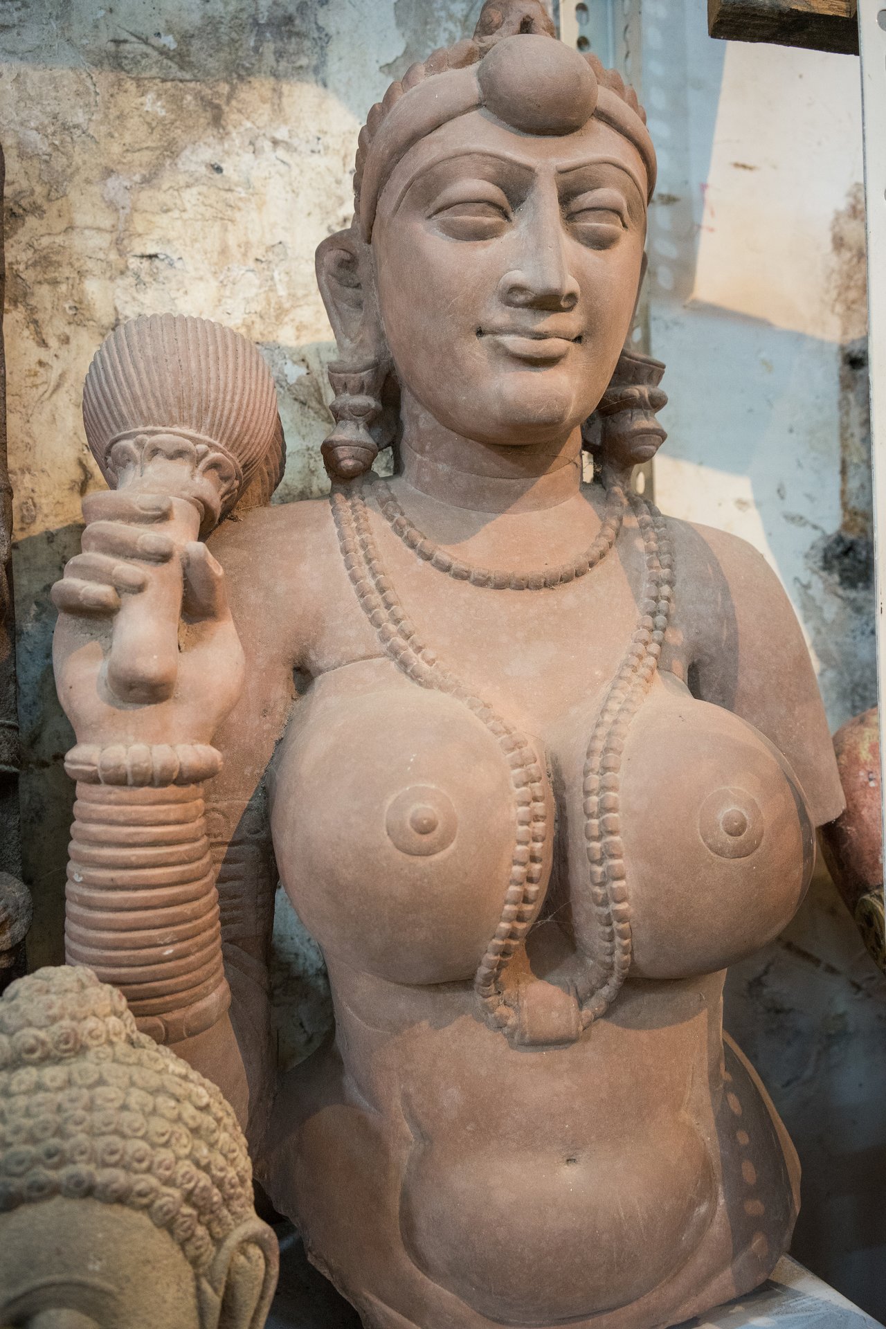 A stone statue of a woman wearing jewelry, holding an object in one hand, with a calm facial expression.