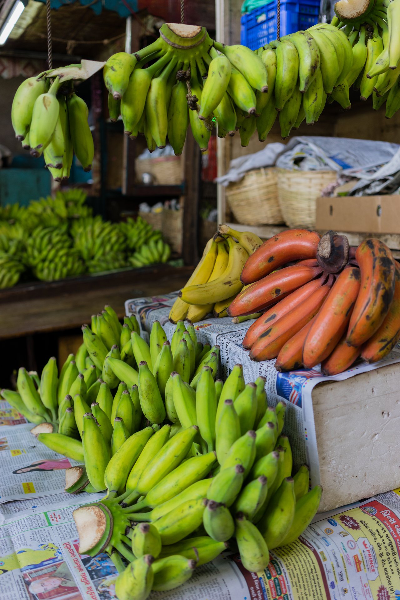 Various types of bananas, including green, yellow, and red, are displayed for sale at a market stall.