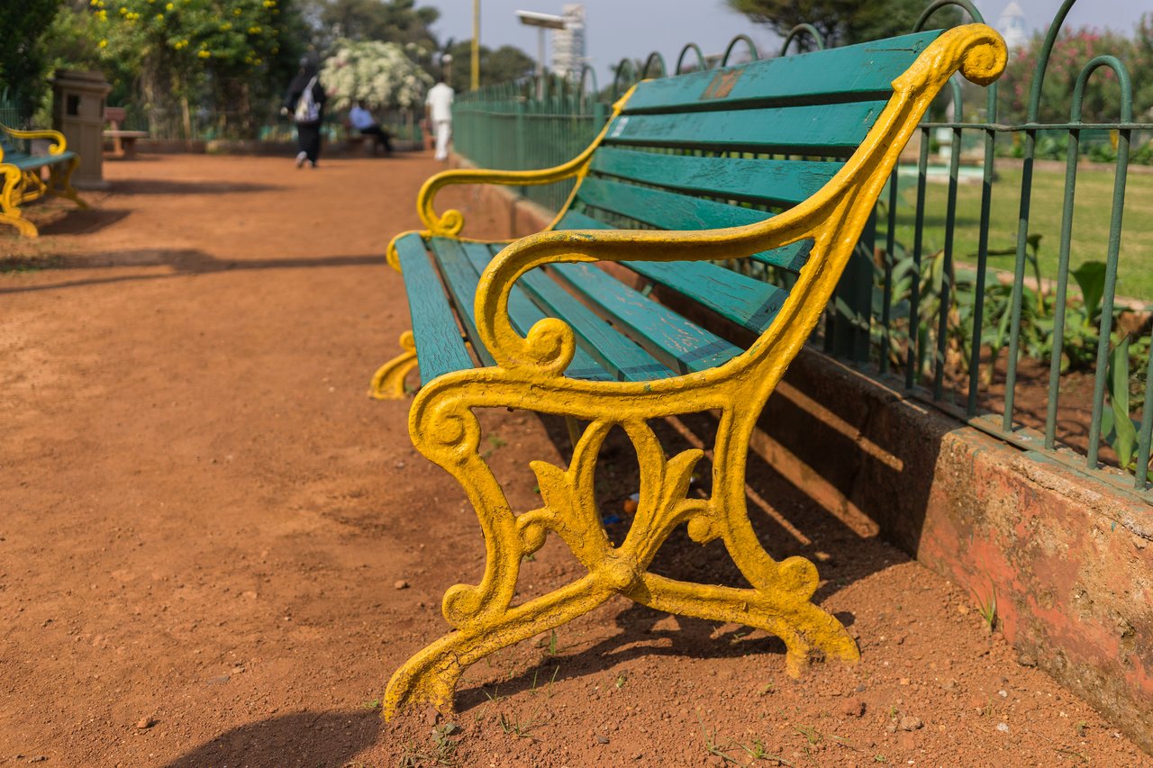 A green and yellow park bench on a dirt path.
