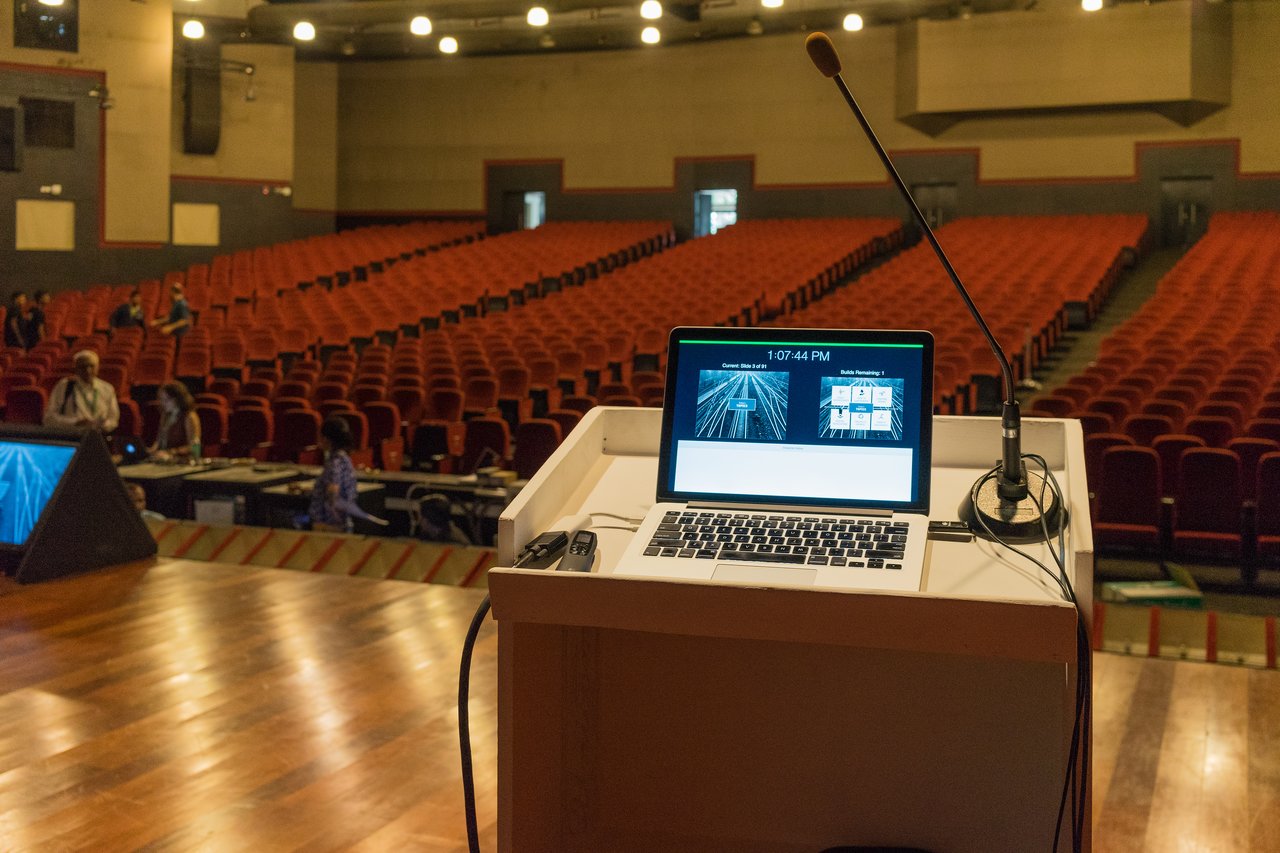 A laptop and microphone on a podium in an empty auditorium, prepared for a presentation or speech.