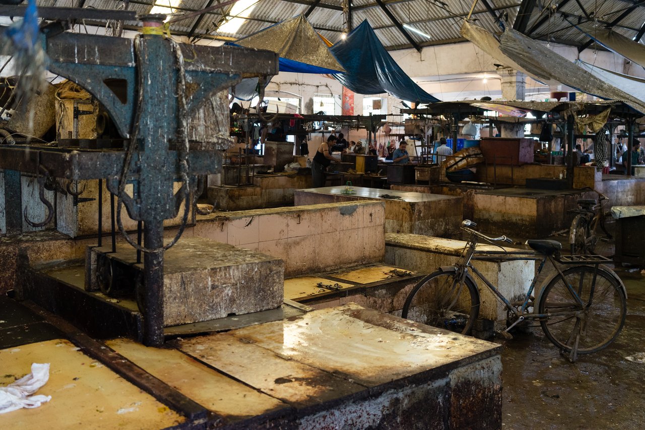 An empty, worn-out fish market with stained countertops, a rusty weighing scale, and a bicycle leaning against a counter.