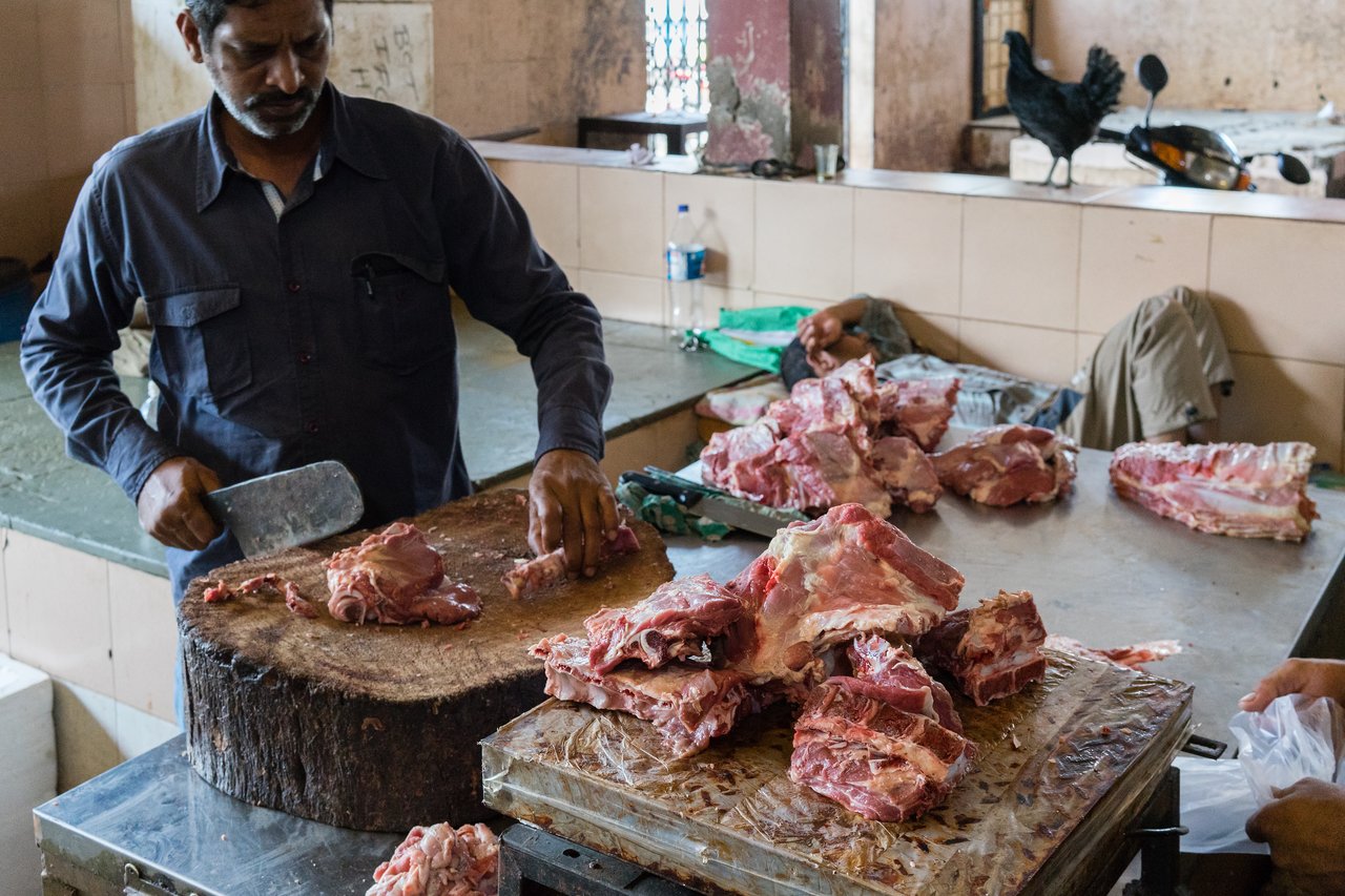 A butcher chops raw meat on a wooden block with a cleaver at a meat market.