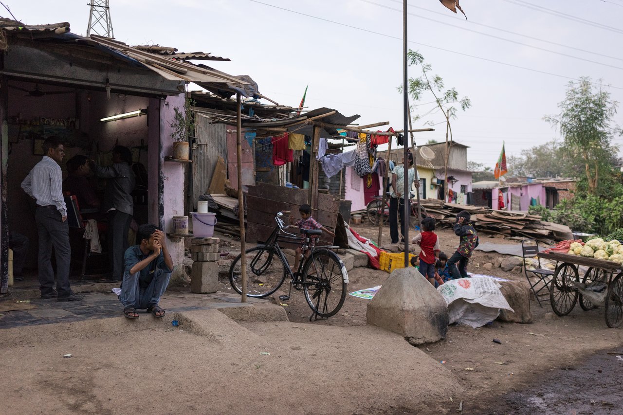 A man sits on a step, his head in his hands, with slums stretching behind him.
