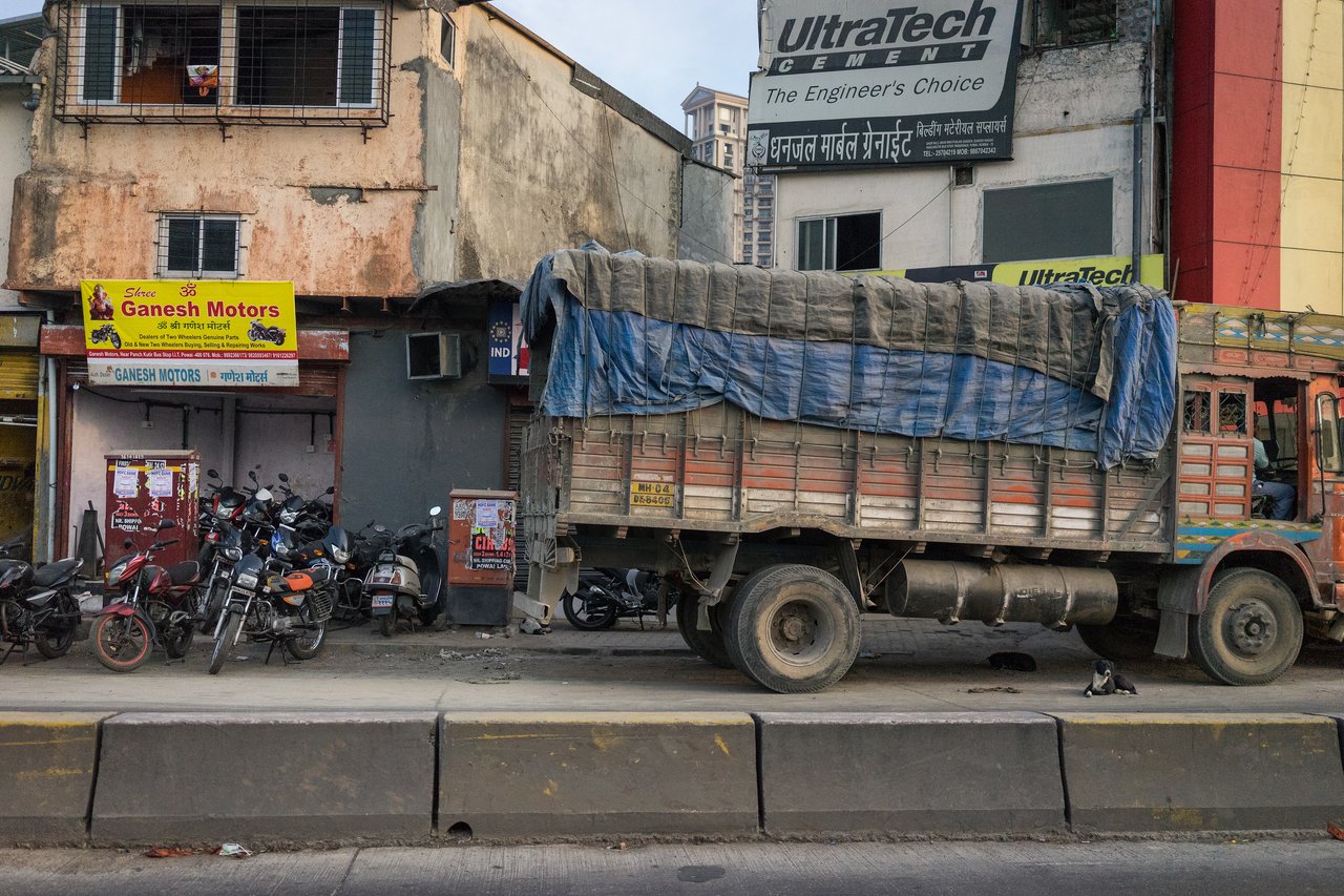 A large truck with a covered cargo bed is parked on the roadside near a motorcycle repair shop.
