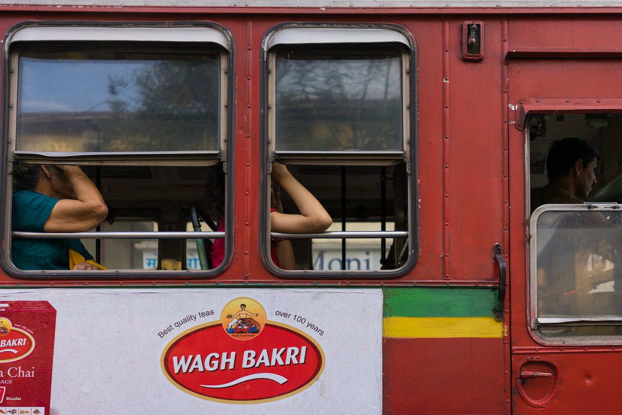 Passengers sit inside a red bus, looking out the windows.