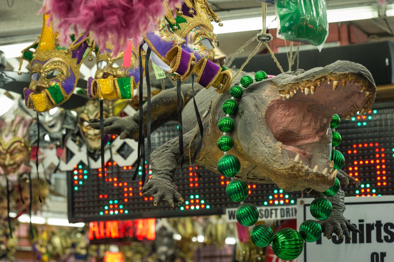 A hanging alligator decoration with an open mouth, wearing large green bead necklaces in a store.