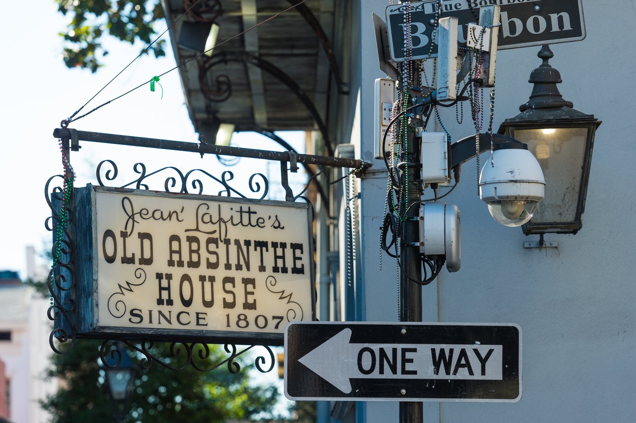A street sign for Bourbon Street, a one-way sign, and a hanging sign for Jean Lafitte's Old Absinthe House.