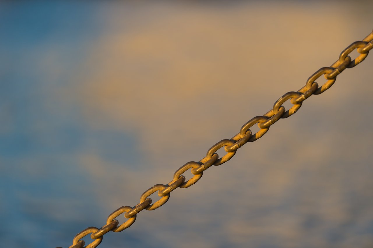 A metal chain stretches diagonally across the image, with a blurred background of blue and yellow tones.