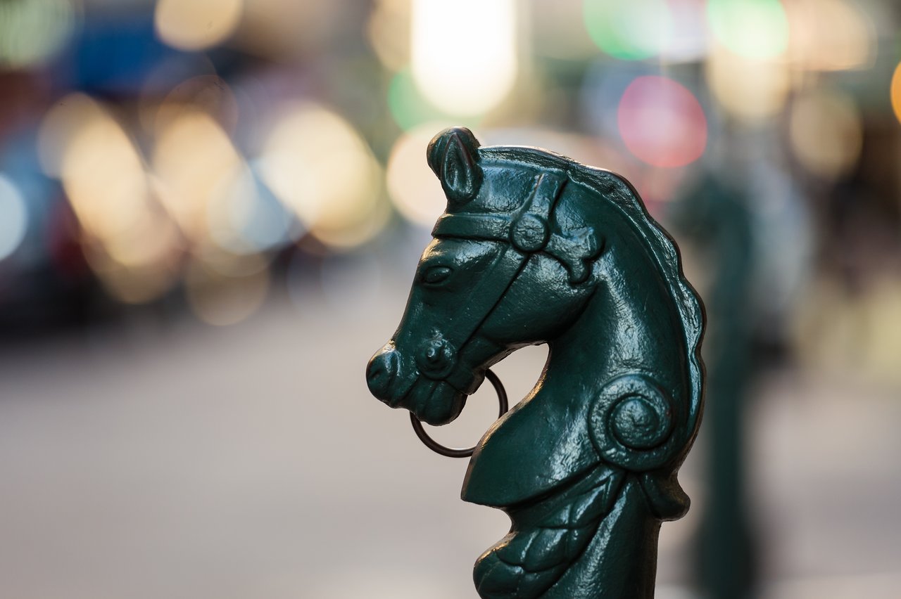 Close-up of a green cast-iron horse head hitching post with a metal ring in its mouth.