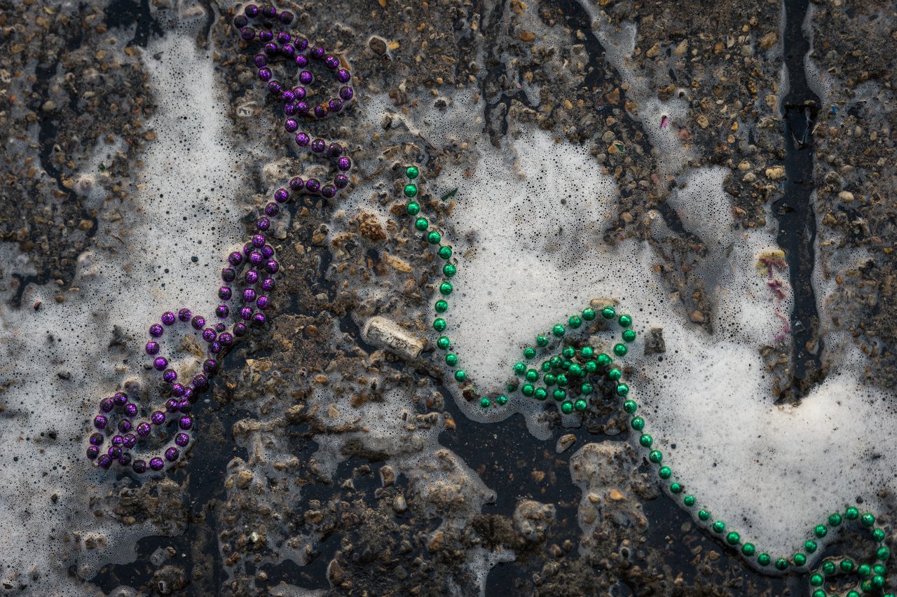 Foamy water washes over purple and green bead necklaces on a rough street surface.