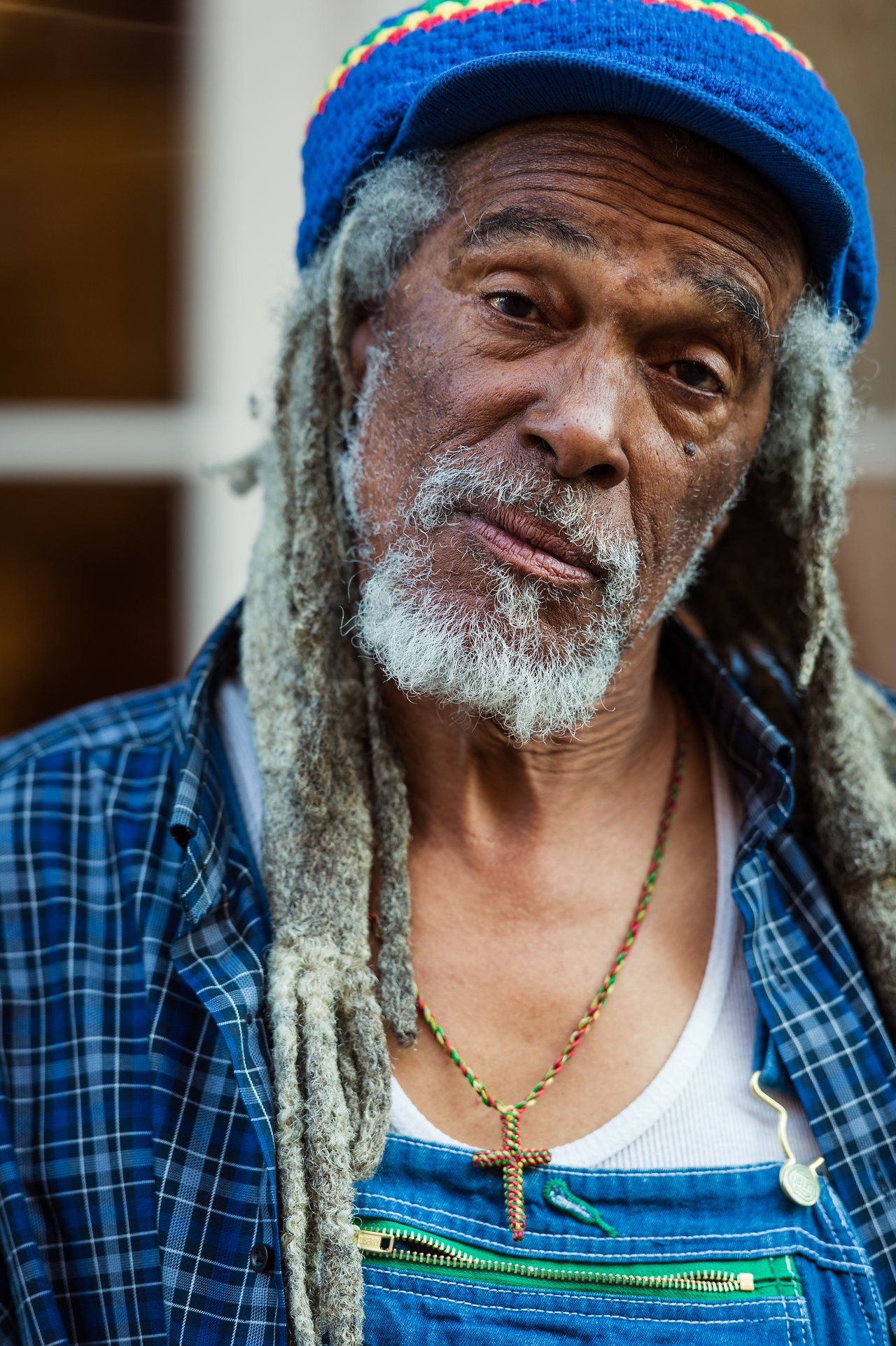 An older man with gray dreadlocks and a blue hat looks directly at the camera with a calm expression.