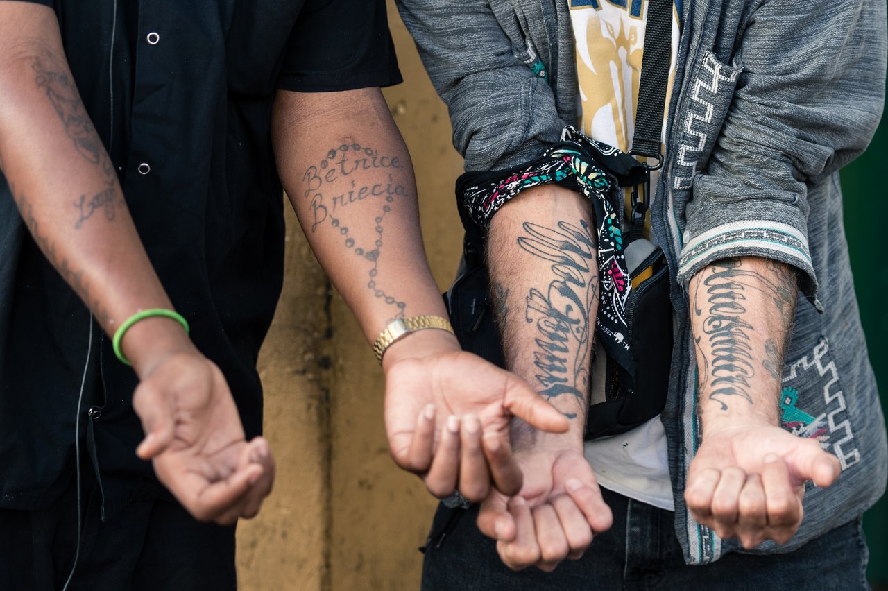 Three people extend their arms, showing tattoos with names and designs on their forearms.