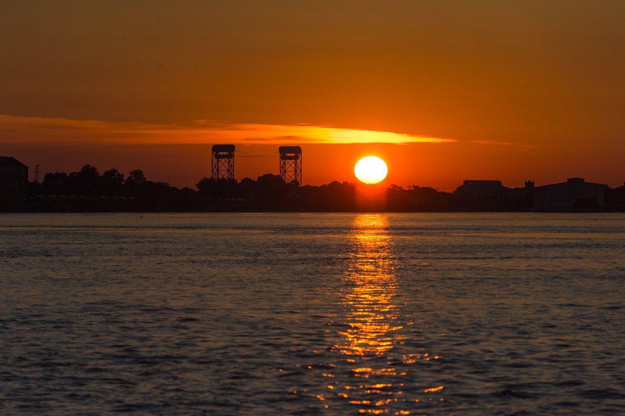 The sun rises over the water, casting a bright reflection.