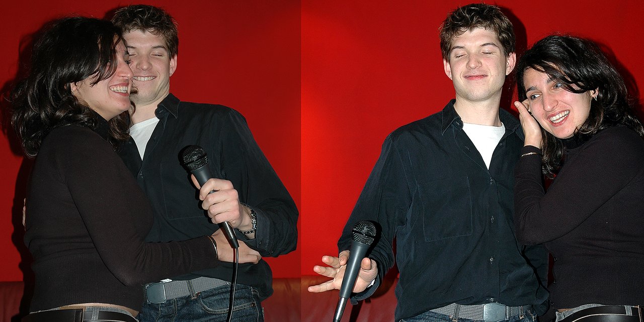 Two people laughing and singing karaoke, one holding a microphone while the other leans in playfully.