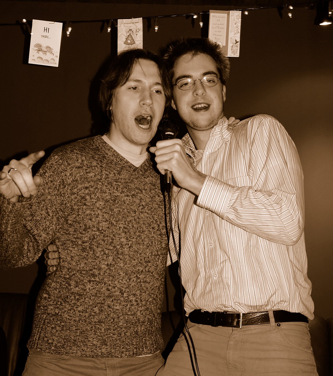 Two people singing karaoke together, sharing a microphone and smiling.