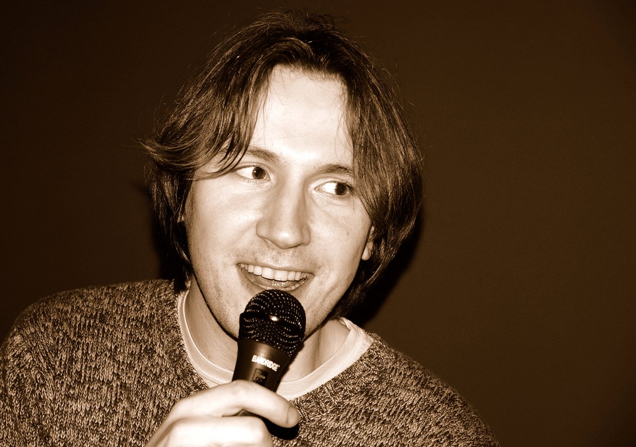 A person holding a microphone and singing karaoke with a smile.