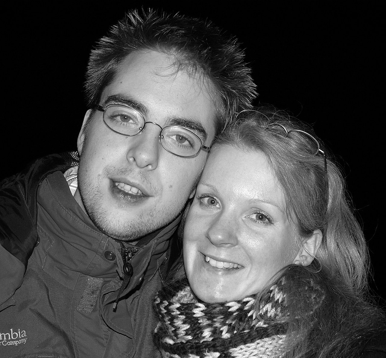 A man and woman smile while posing closely together, dressed in warm clothing.