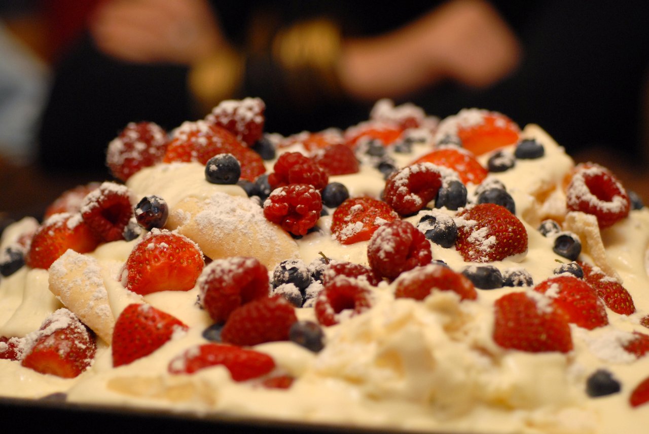 A dessert topped with whipped cream, fresh strawberries, raspberries, blueberries, and powdered sugar on a plate.