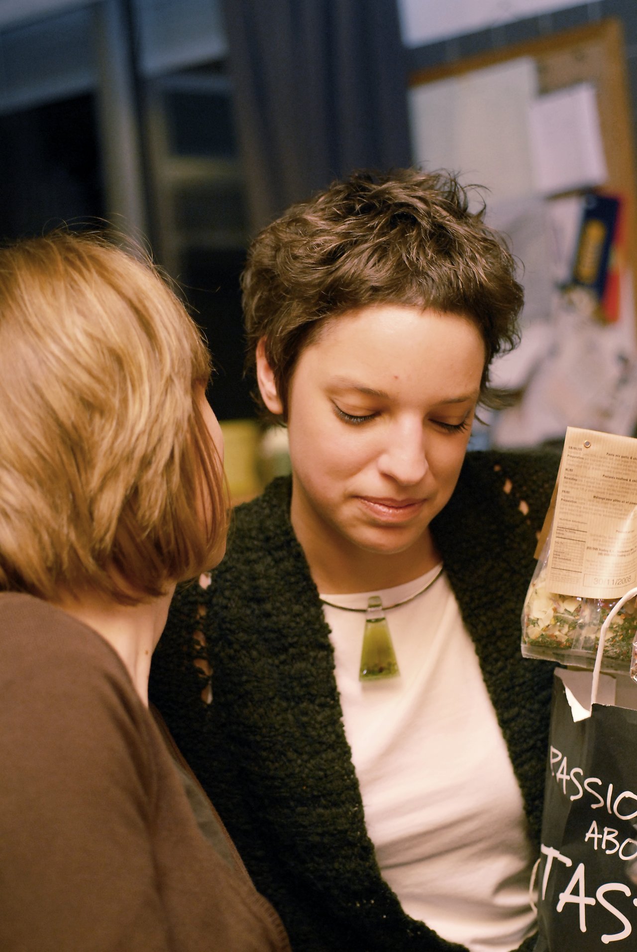 Two people in conversation, one looking down while holding a bag with a visible label.