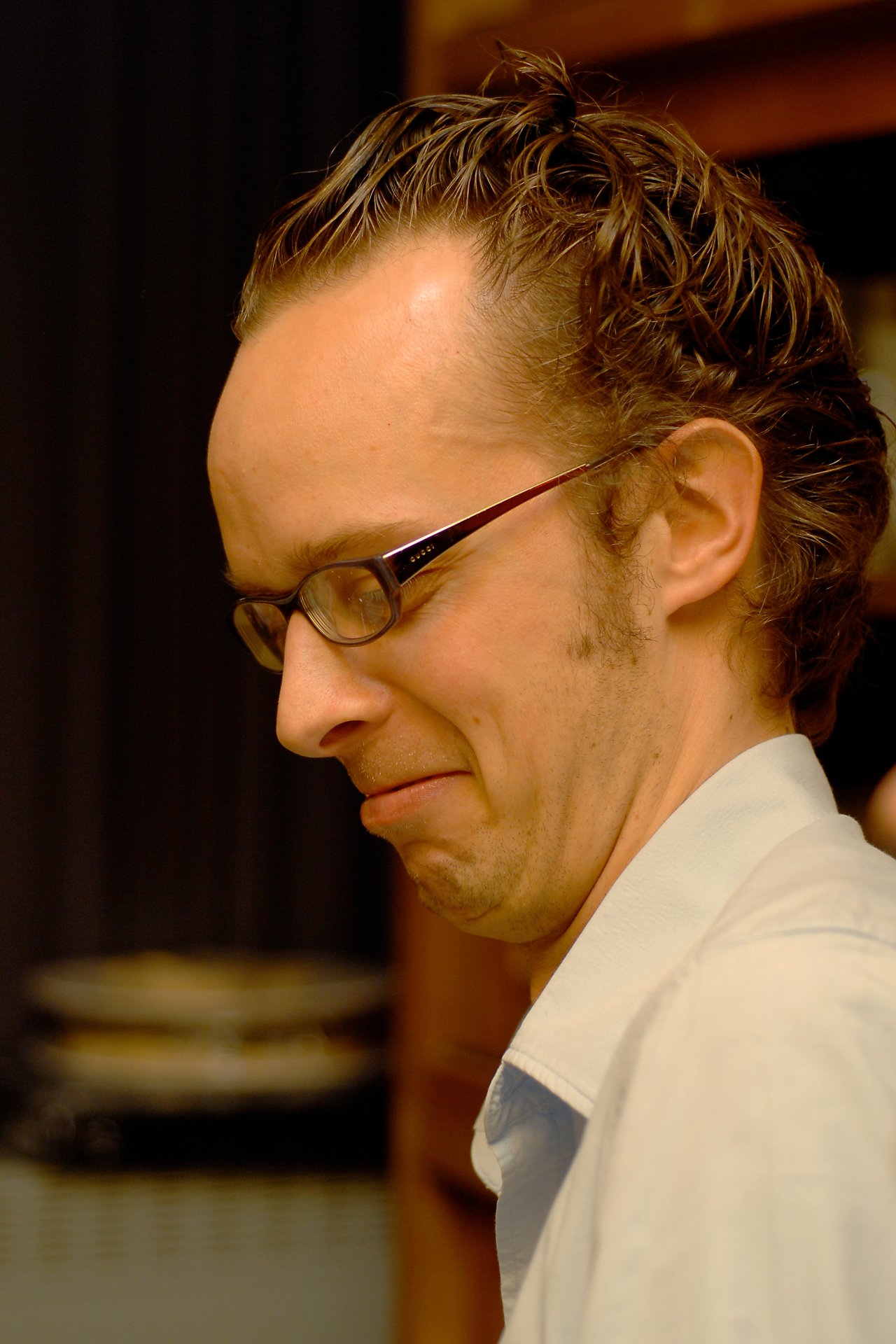 A man wearing glasses and a light-colored shirt makes a facial expression, possibly reacting to something.