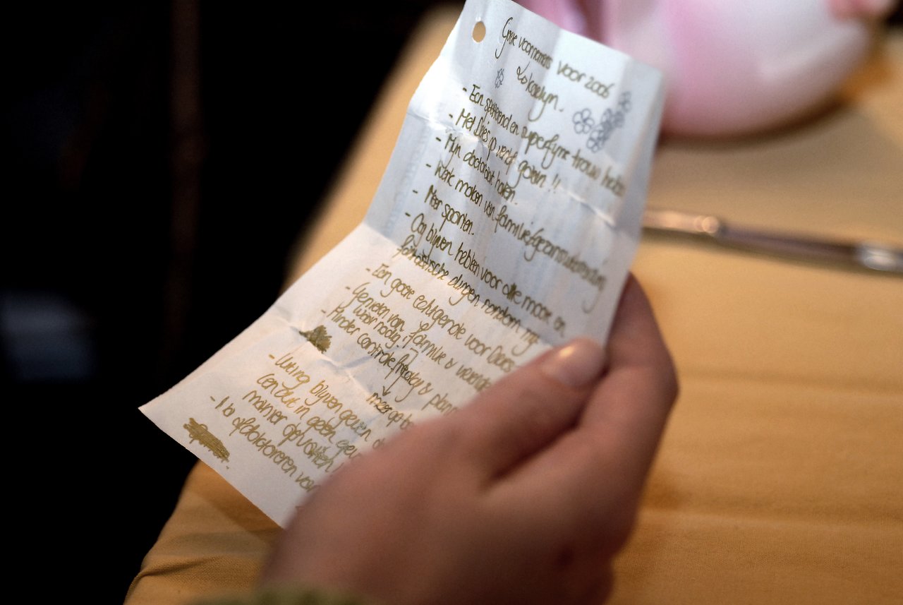 A person holds and reads a handwritten list of New Year's resolutions on a crumpled piece of paper.