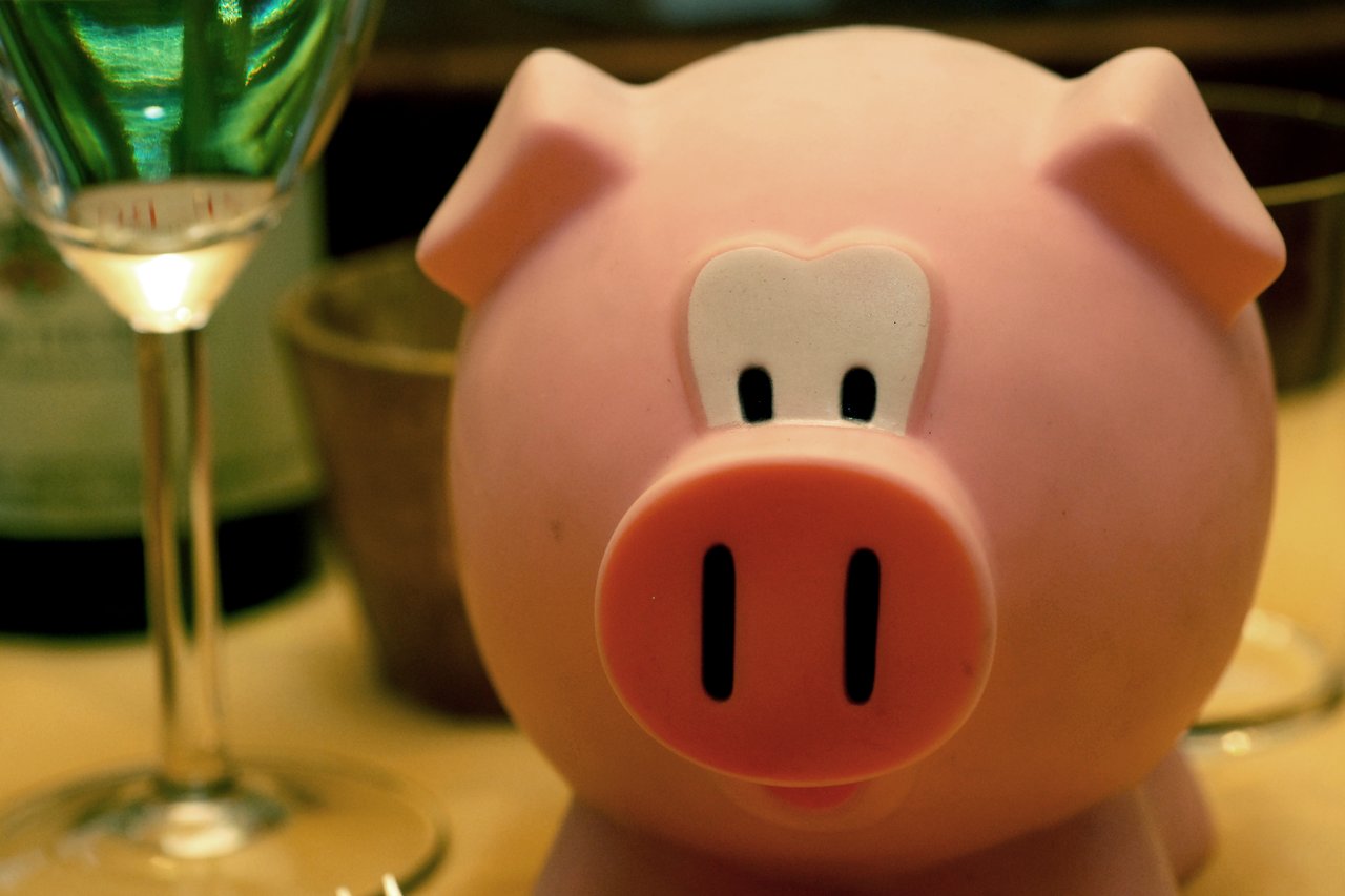 A pink pig-shaped container used to store New Year's resolutions, placed on a table with glasses nearby.