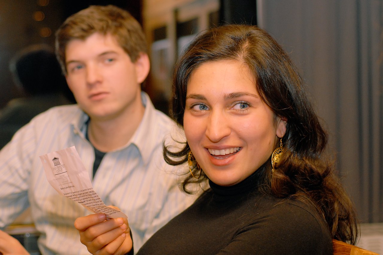 A smiling woman in a black top holds a piece of paper, while a man in a striped shirt looks on.