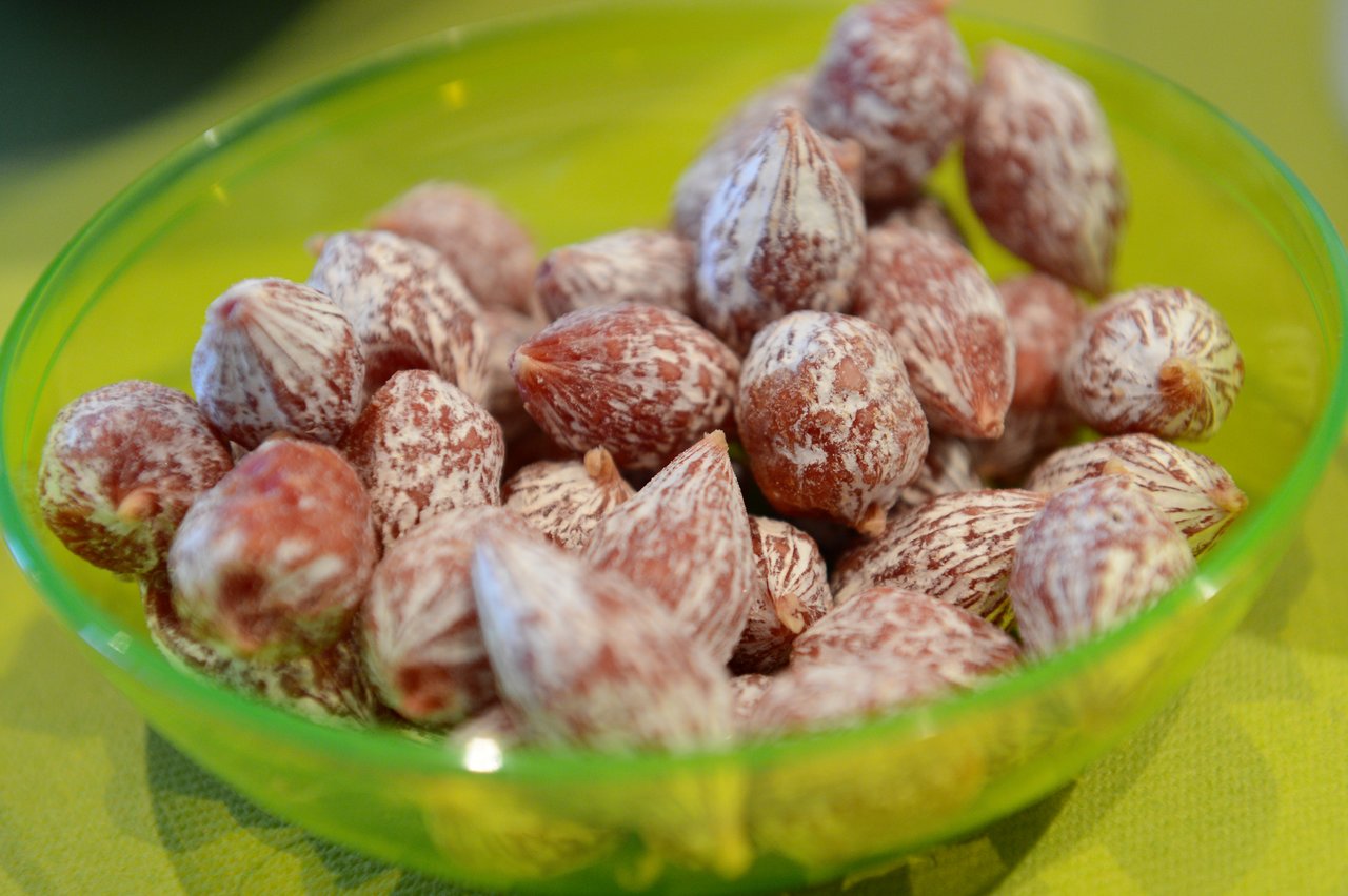 A green bowl filled with coated nuts or seeds, placed on a table.