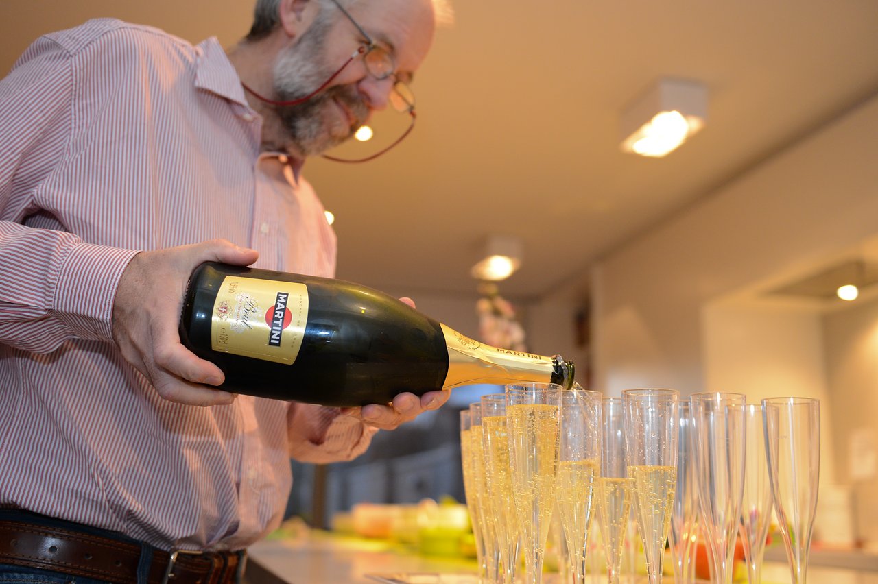 A person pours sparkling wine into multiple champagne glasses at a party.