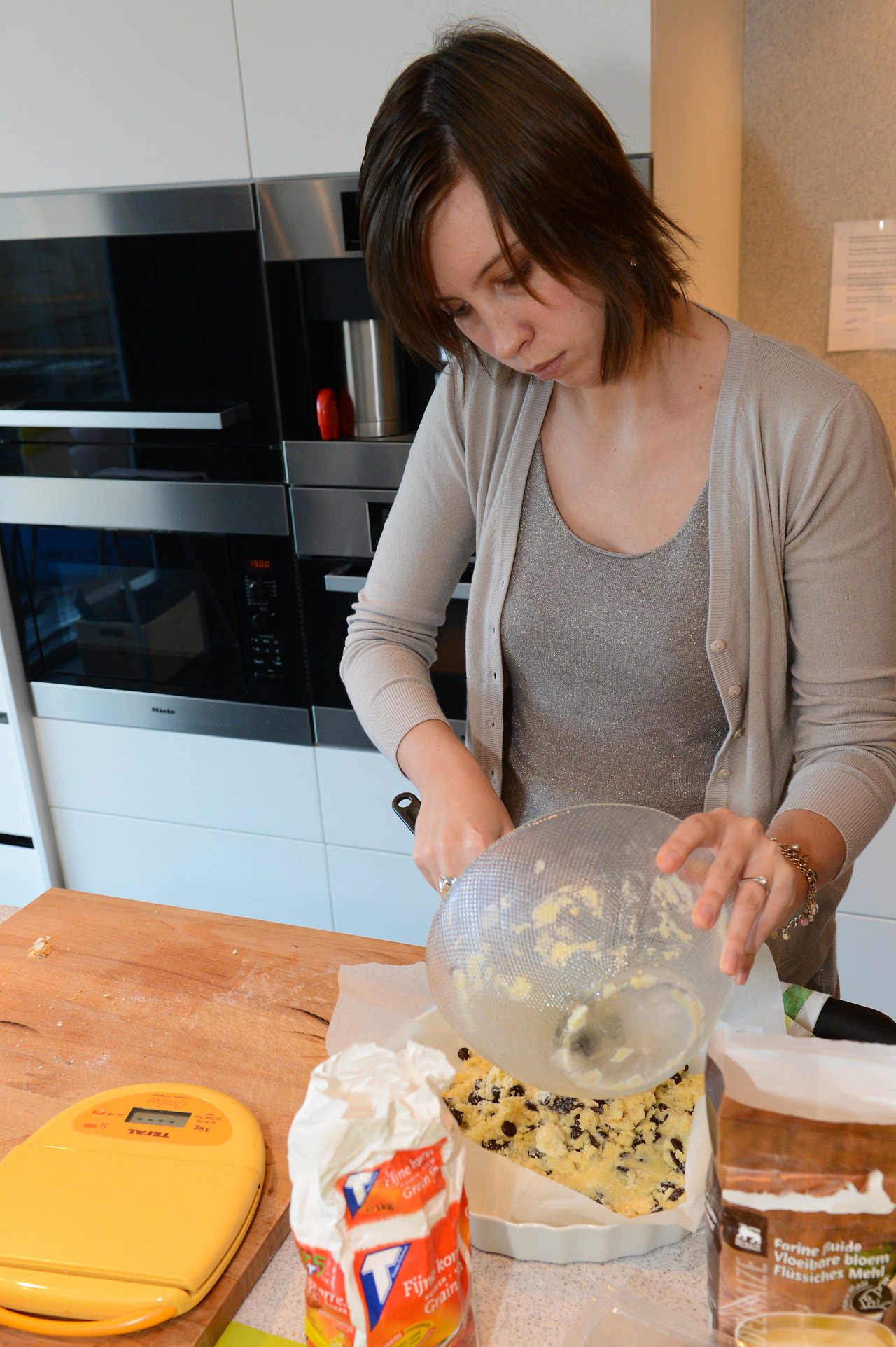 A woman pours cake batter with raisins into a baking dish in a kitchen.