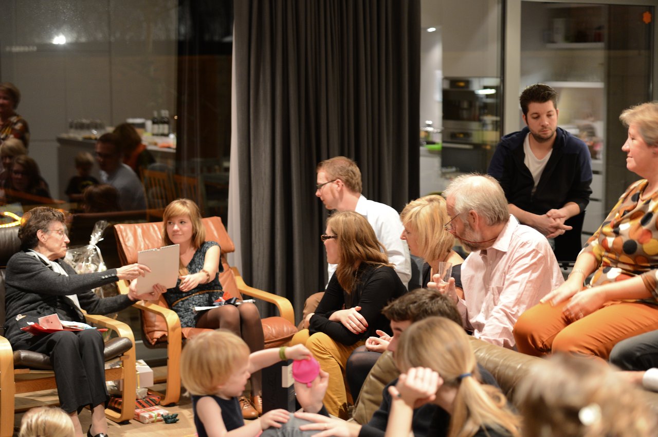 A group of people gathers indoors, talking and exchanging gifts during a New Year's party.