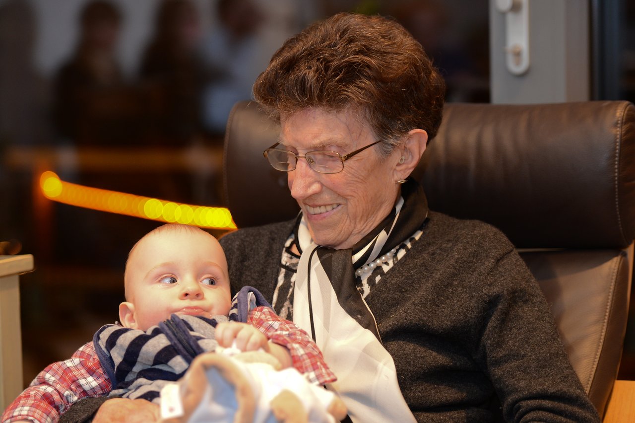 An elderly woman smiles while holding a baby in her arms at a New Year's party.