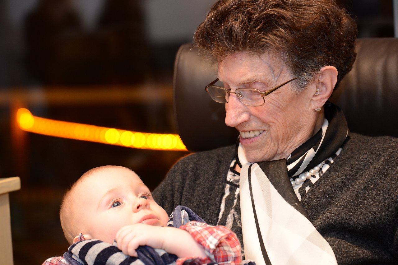 An elderly woman smiles while holding a baby in her arms at a New Year's party.